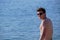 A young man 25-30 years old European appearance on the beach against the background of the sea  looks into the lens  smiles  naked