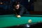 Young man aiming to take snooker shot in dark club