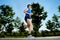 Young man with athletic runner legs holding isotonic energy drink while running in city park