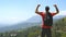 Young man with backpack reaching up top of mountain and raised hands. Male tourist standing on the edge of beautiful