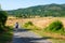 A young man with backpack is walking on a natural Tuscan landscape with a road through the fields, sunny day in June 2019, Italy