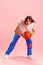 Young man basketball player in retro sport uniform stands on attack training technique holding ball against pastel pink