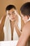 Young man in the bathroom\'s mirror after shaving