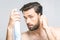 Young man with a beard on a grey isolated background purrs a hair spray. Beauty concept