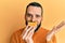 Young man with beard holding orange slice on mouth as funny smile celebrating achievement with happy smile and winner expression