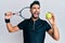 Young man with beard playing tennis holding racket and ball angry and mad screaming frustrated and furious, shouting with anger