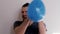 Young man with beard and ponytail of Caucasian European appearance tries to burst blue balloon with both hands, but he fails and b