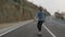 Young man with a beard riding skateboard cruising downhill on countryside road