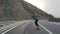 Young man with a beard riding skateboard cruising downhill on countryside road