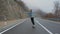 Young man with a beard riding skateboard cruising downhill on countryside road