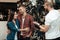 A young man with a beard shows a man and a woman a wheel from a bicycle in a bicycle shop.