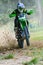 Young man in a black and green leather jacket and helmet is riding a dirt bike off-road.