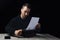 Young man in black hoodie inserts paper into typewriter on black background in low key