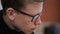 Young man in black-rimmed glasses with a serious face pimples, and reflection of laptop screen, close up.