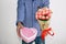 A young man in a blue plaid shirt and jeans, holding out a bouquet of tulips and a heart-shaped gift box, on a white background.