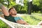 Young man with book resting in comfortable hammock at garden