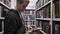 Young man in a bookstore holding an opened book in his hands with other bookshelves on the background, education and