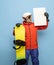 Young man in bright ski suit and snowboard posing isolated on blue background.