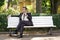 A young man in a business suit left the office and came to the Park. he sits on a white bench alone and talks on the phone