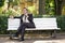 A young man in a business suit left the office and came to the Park. he sits on a white bench alone and talks on the phone