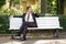 A young man in a business suit left the office and came to the Park. he sits on a white bench alone and talks on the phone