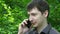 Young man call using cell smart phone smiling outdoors handsome guy talking closeup over green trees slow motion