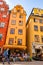 Young man with camera walking by cozy medieval street with people sitting in outdoor restaurant, high vibrant buildings facades in