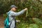 A young man in a cap with a backpack behind him on a walk through the unique enaga forest of Anaga. Holds a lichen in his hand.