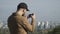 Young man in cap makes a panorama photo of city at smartphone