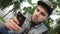 Young man in cap sit with phone in hands. Typing. Summer day. Communication