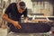 Young man in carpentry workshop fixing wheel on his skateboard