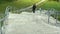 A young man carries a bicycle through the long stairs. Against the background of green field. Clouds changing light