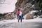 Young man carries his girlfriend on back across puddle of melted water. Couple laughs.