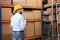 Young man with clipboard near rack of boxes at warehouse, back view