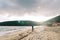 Young man with a colorful kite soaring in the sky walks along a sandy beach. Back view