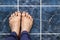 Young man crossing feet on square tiles. Veins in feet visible.