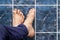 Young man crossing feet on square tiles. Veins in feet visible.