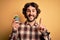 Young man with curly hair and beard holding small cactus plant pot over yellow background surprised with an idea or question