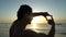 Young man with curly hair making photo frame with his hands at amazing sunset on the beach. Silhouette of photographer