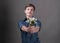 Young man with dark hair in blue shirt smile, holding bouguet with flowers in outstreched hands and looking at camera