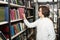 Young man with dark hair choosing a book standing between shelve