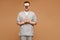 Young man doctor in medical uniform and glasses keeps surgeon tools in hands and posing at the beige background