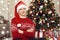 Young man dressed in retro sweater and sanat hat sit near christmas tree. New year eve, ornated fir tree. Winter holiday and love