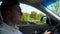 Young man driving a car passing farm buildings