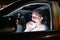 Young man eating burger in the car driving late at night in the parking lot