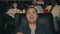 Young man eating popcorn and drinking orange juice in cinema watching film