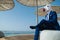 Young man in elegant suit sits under stylish umbrellas on the city waterfront