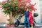 Young man embracing girlfriend with tenderness sitting on scooter parked under blooming bougainvillea tree on the mediterranean ci