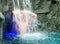 Young man enjoys the falling water under the splashing waterfall with blue light