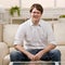 Young man in eyeglasses sitting on sofa at home